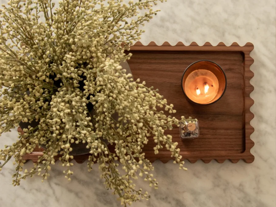 Scalloped walnut tray with a lit candle and dried flowers on a marble surface
