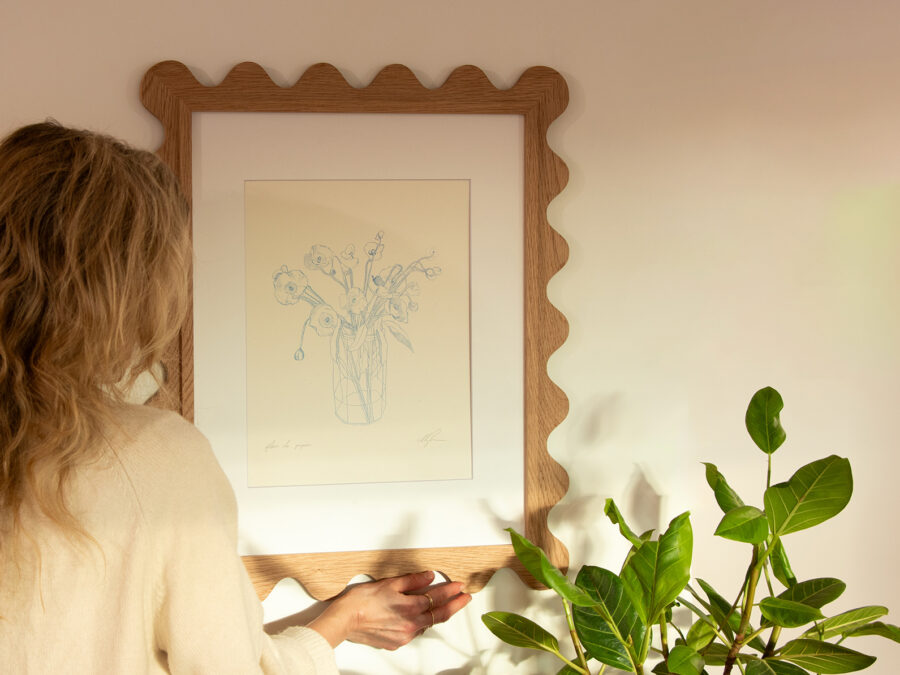 Woman hanging a scalloped oak picture frame with a botanical sketch print