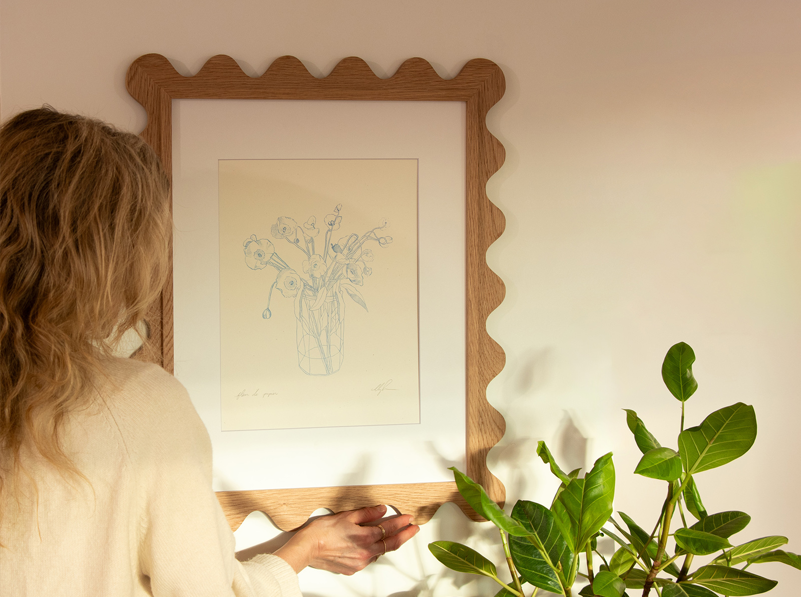 Woman hanging a scalloped oak picture frame with a botanical sketch print