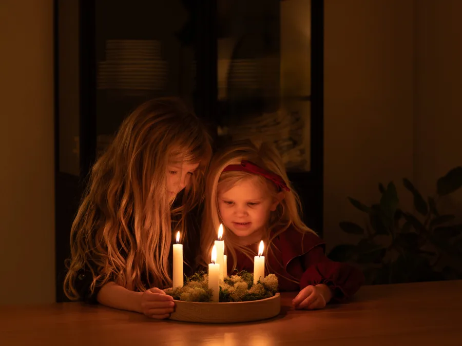 Two girls looking at lit candles in a round wooden advent holder with moss